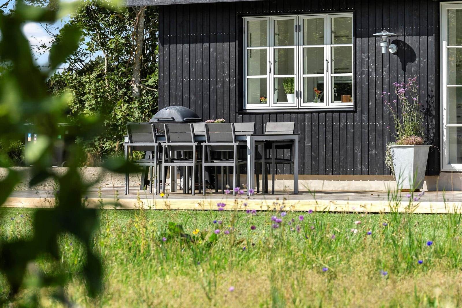 Terrasse mit Tisch, Stühlen und Grill vor schwarzem Holzhaus.