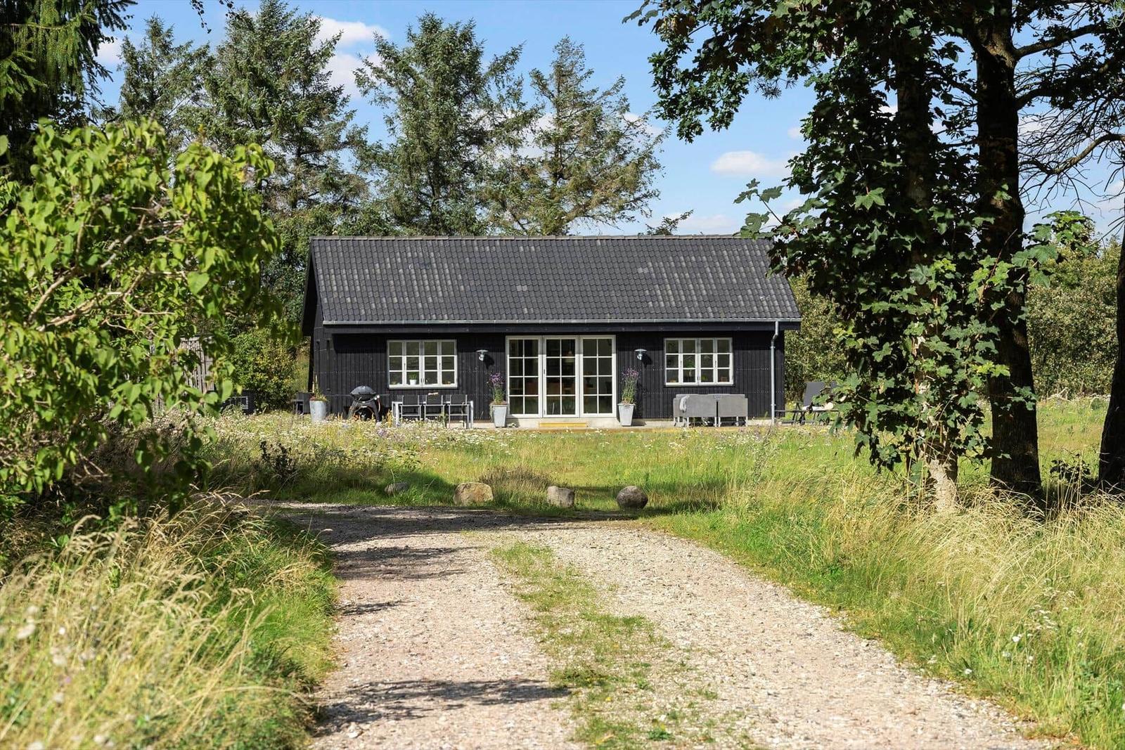 Ein schwarzes Haus mit weißen Fenstern und einer Terrasse im Grünen.