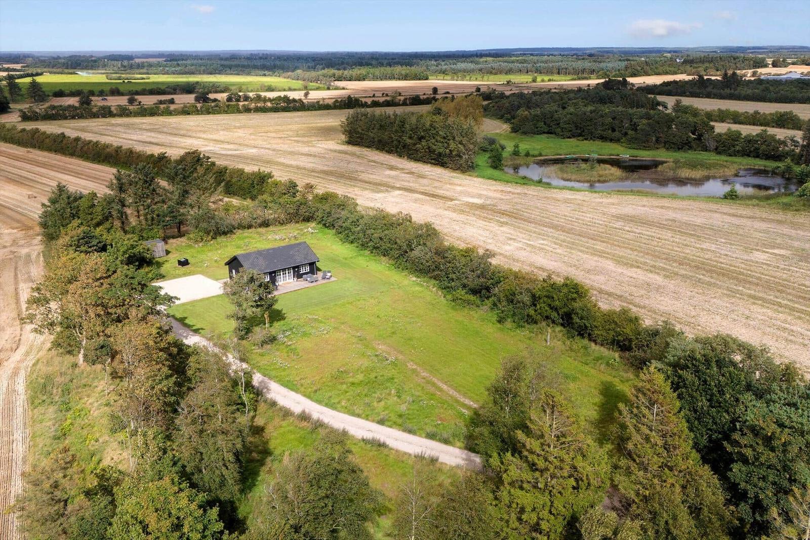 Ein Haus mit Terrasse steht in einer grünen Umgebung mit Feldern und einem See.