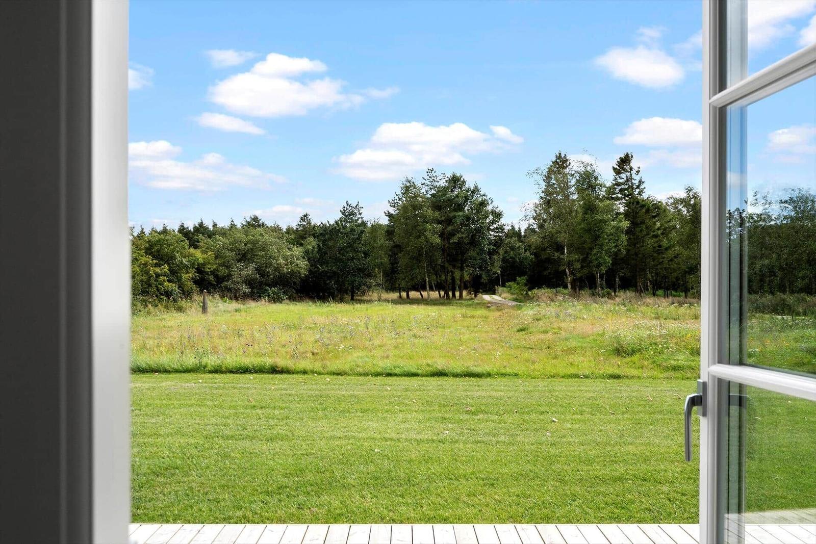 Durch die offene Tür blickt man auf eine grüne Wiese und einen Wald unter blauem Himmel.