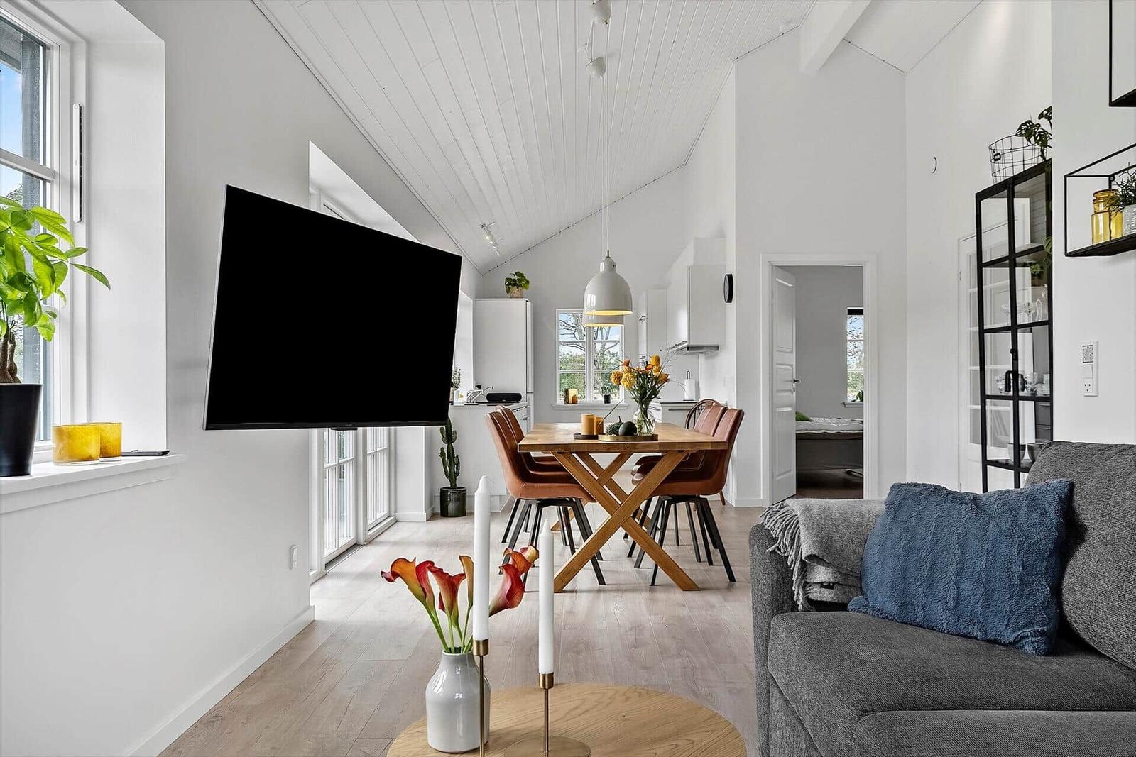 Wohn- und Essbereich mit Fernseher, Tisch und Sofa. Küche im Hintergrund.