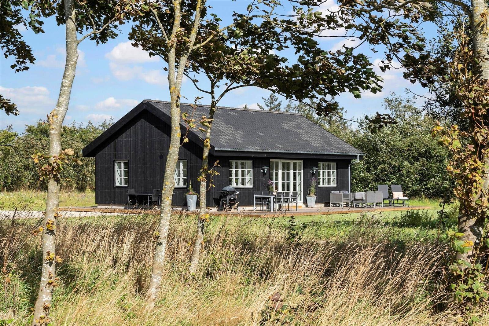 Schwarzes Haus mit Terrasse und Garten unter Bäumen.