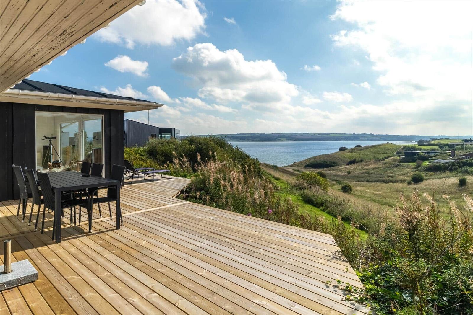 Terrasse mit Tisch und Stühlen bietet Blick auf See und Hügel.