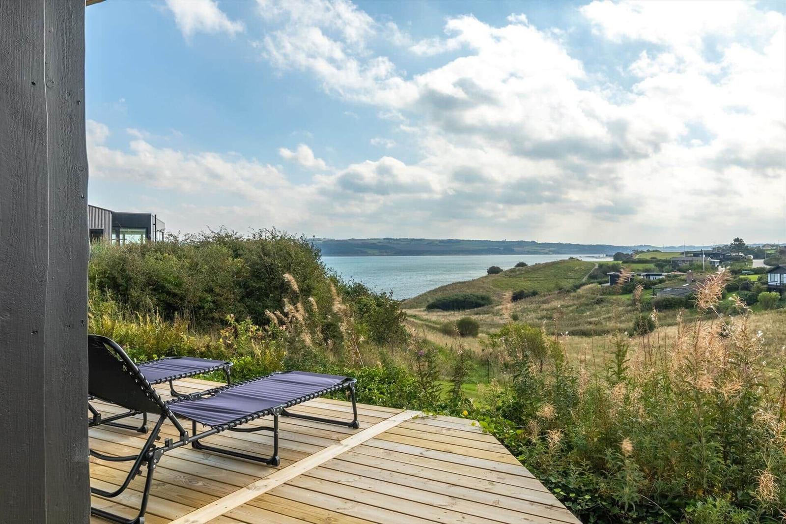 Terrasse mit Liegestühlen und Blick auf See und Hügel.