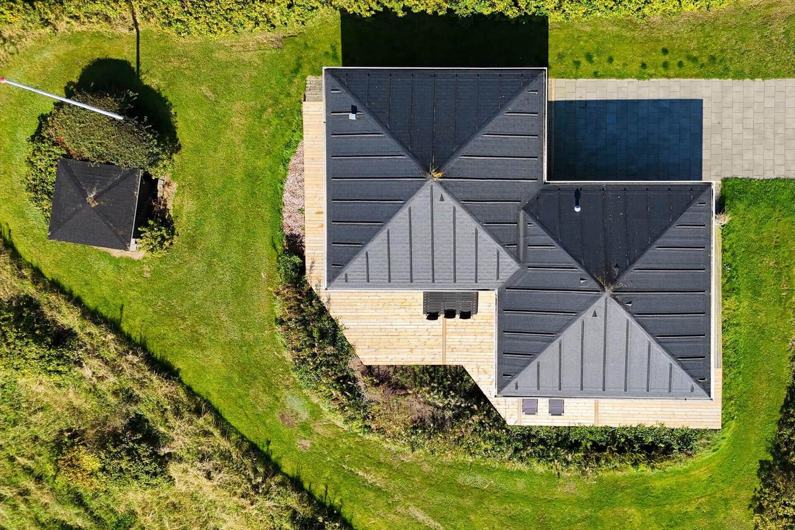 Haus mit schwarzem Dach und umliegenden Grünflächen von oben gesehen.