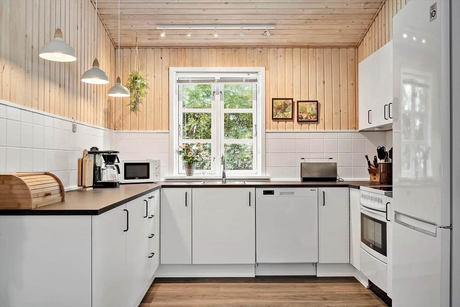 Küche mit weißen Schränken, Holzwand und Fenster mit Blick auf Grün.