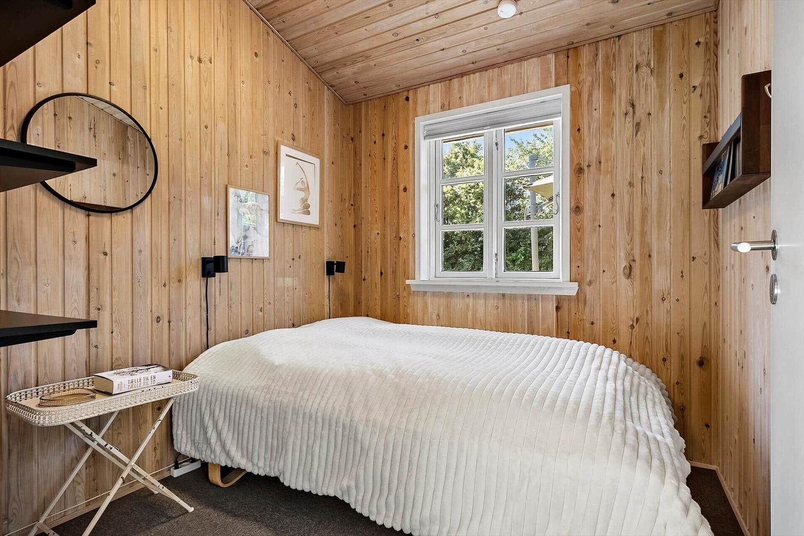 Schlafzimmer mit Holzwand, Bett und Fenster.