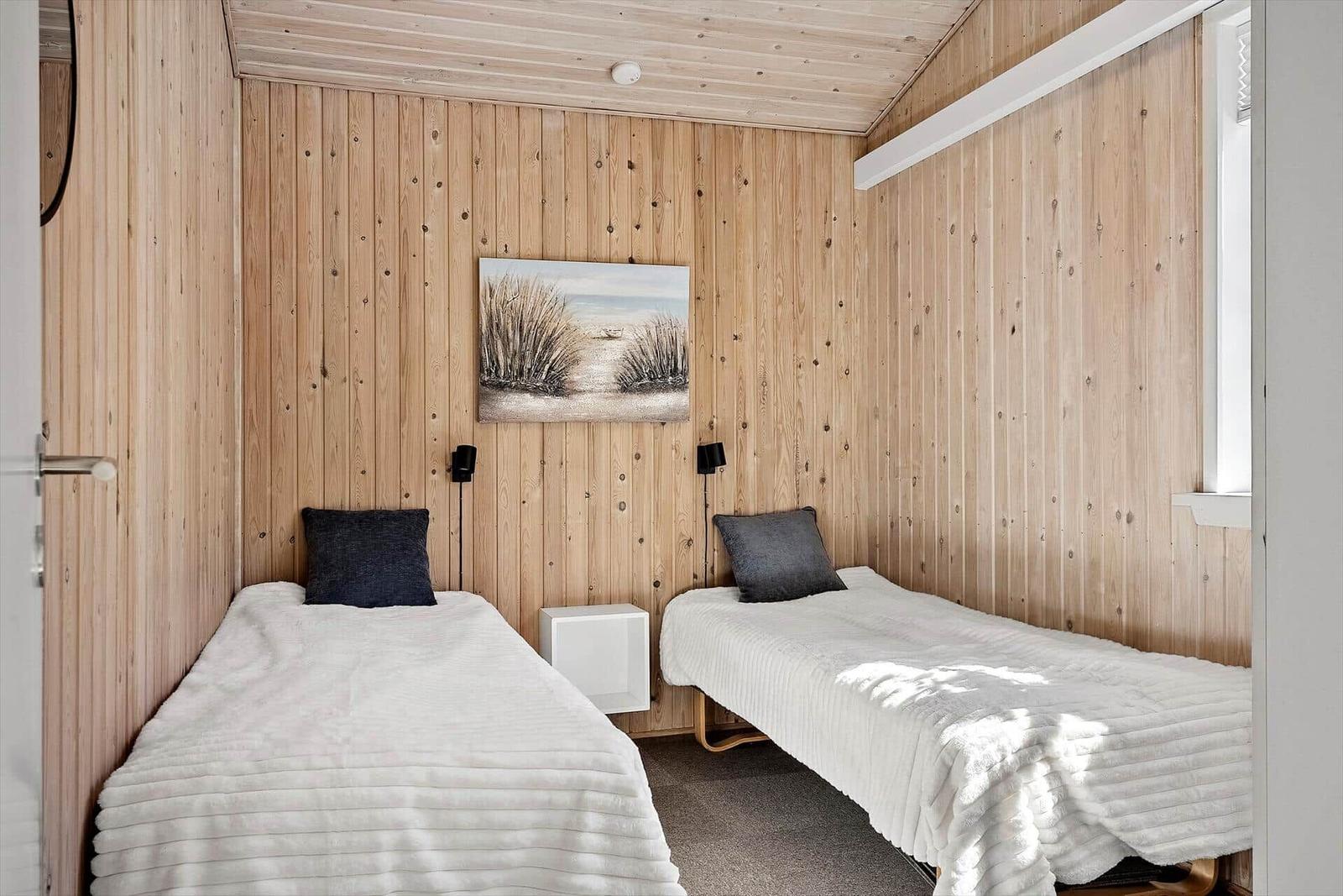 Zwei Einzelbetten mit weißen Bettwäsche und dunklen Kissen an Holzwand.