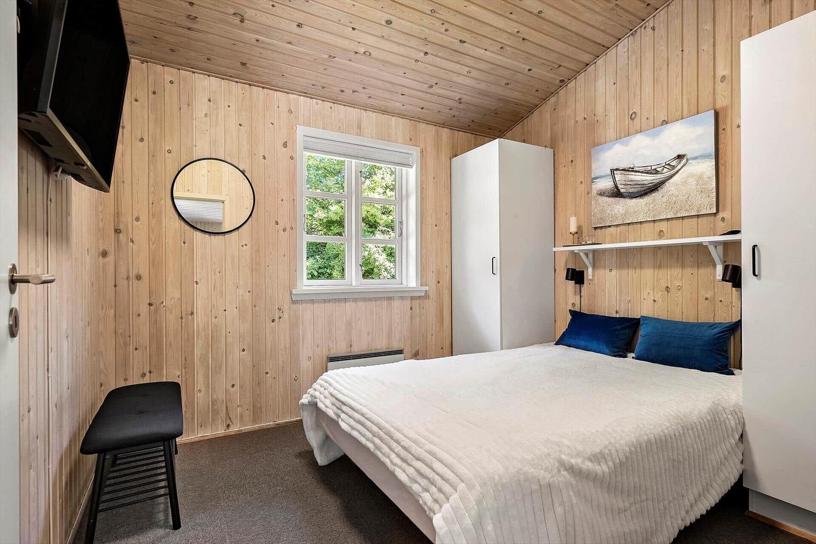 Schlafzimmer mit Holzwand, Bett, Fenster und Schrank.