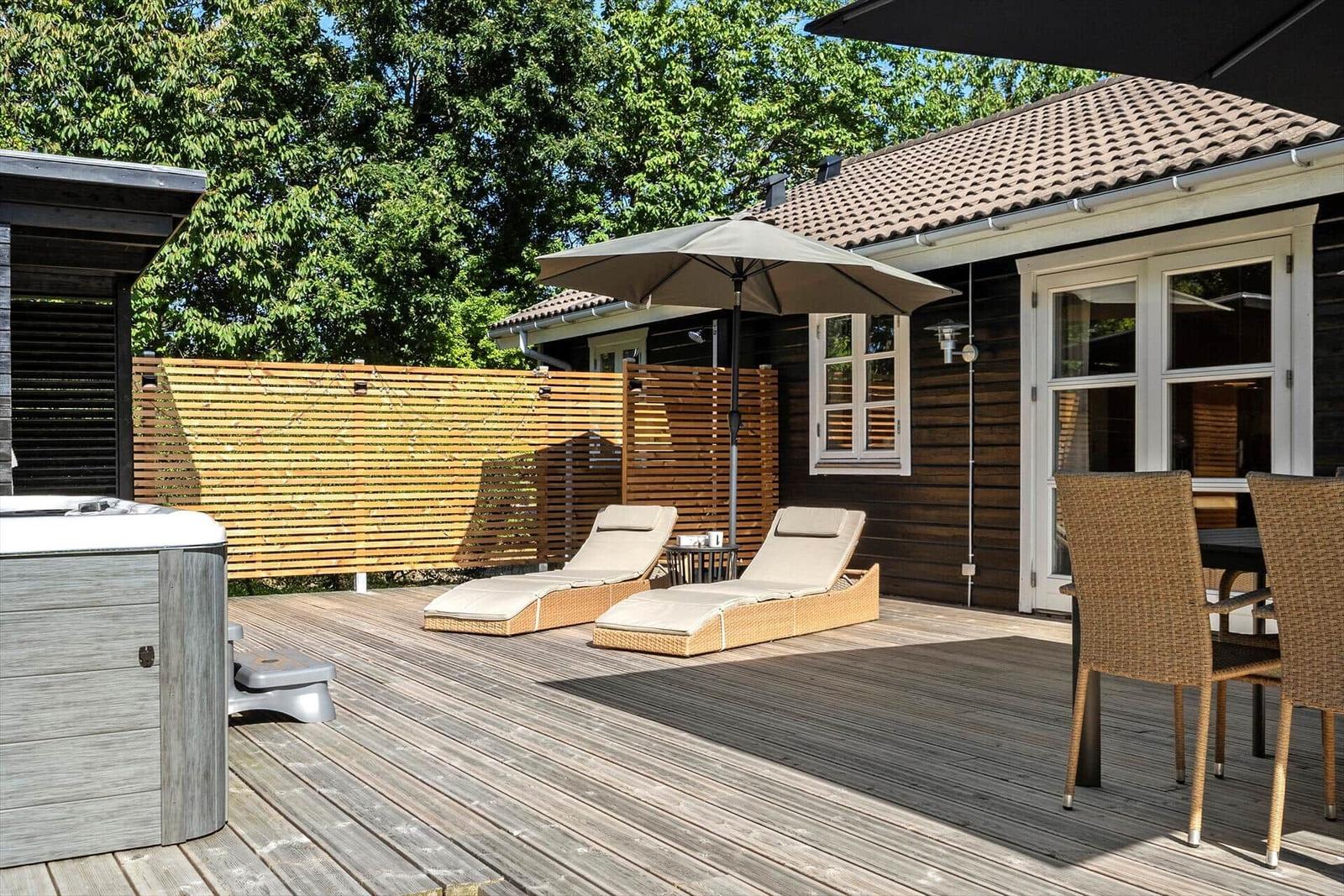 Terrasse mit Liegestühlen, Sonnenschirm und Whirlpool. Holzwand und Holzdecke.