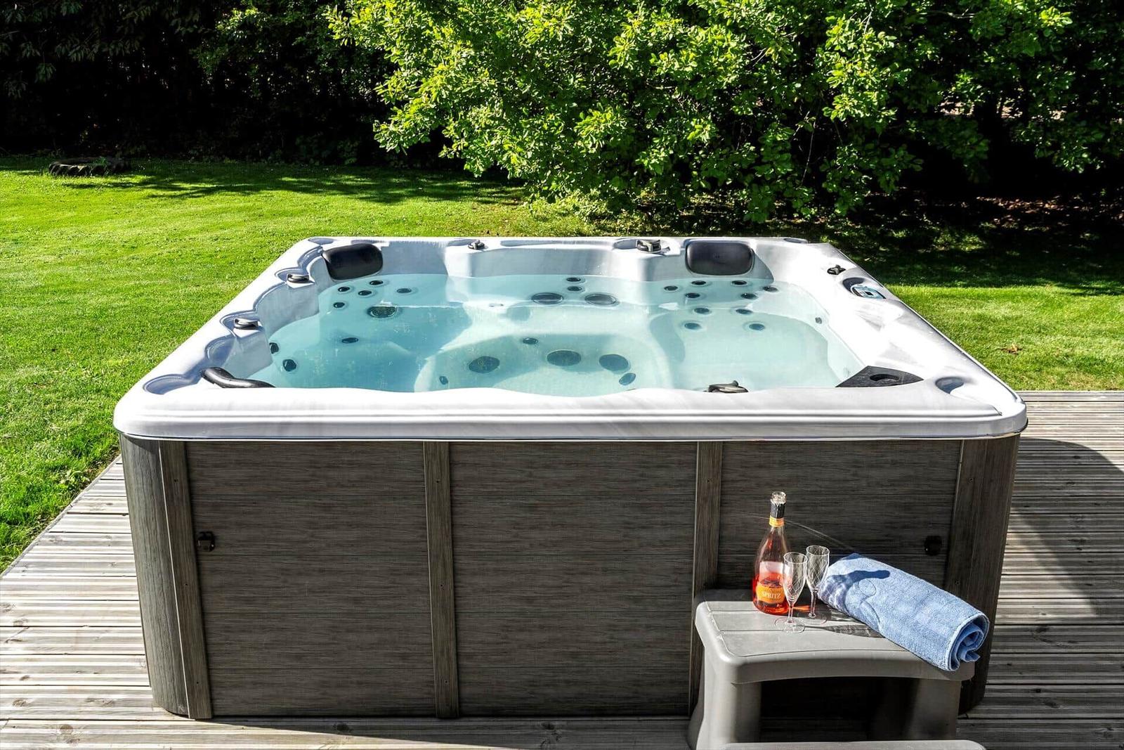 Hochwertige Whirlpool mit Getränk und Handtuch auf Holzterrasse im Grünen.