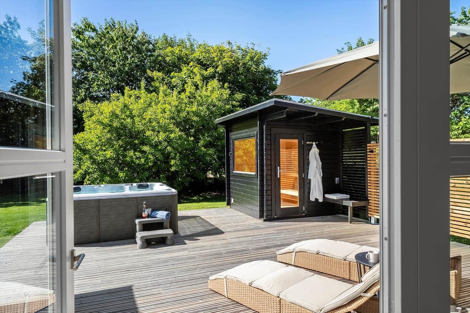 Außenbereich mit Whirlpool, Sauna und Liegen auf Holzterrasse.