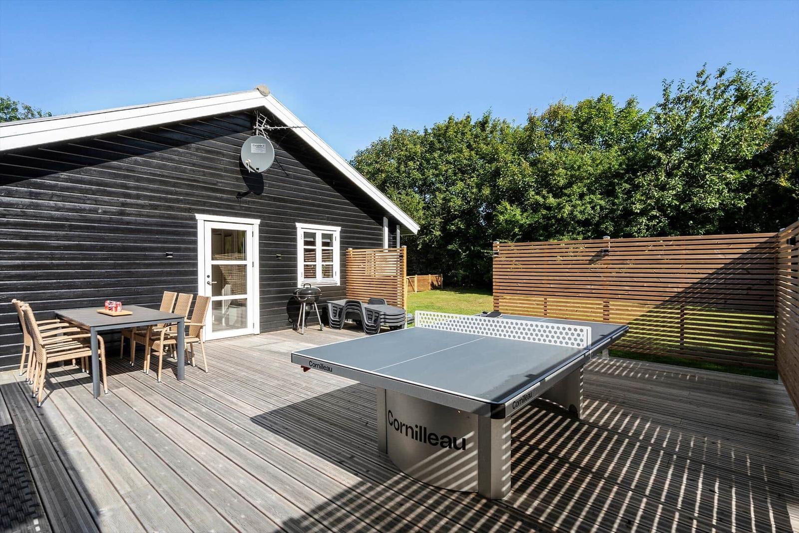 Terrasse mit Tischtennisplatte, Grill und Sitzgruppe vor einem Holzhaus.