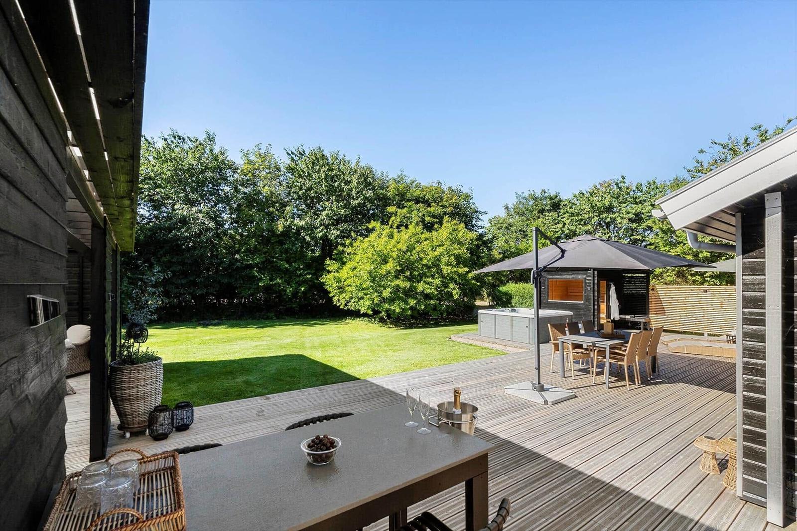 Terrasse mit Grill, Sitzgelegenheiten und Garten. Hintergrund: grüner Rasen und Bäume.