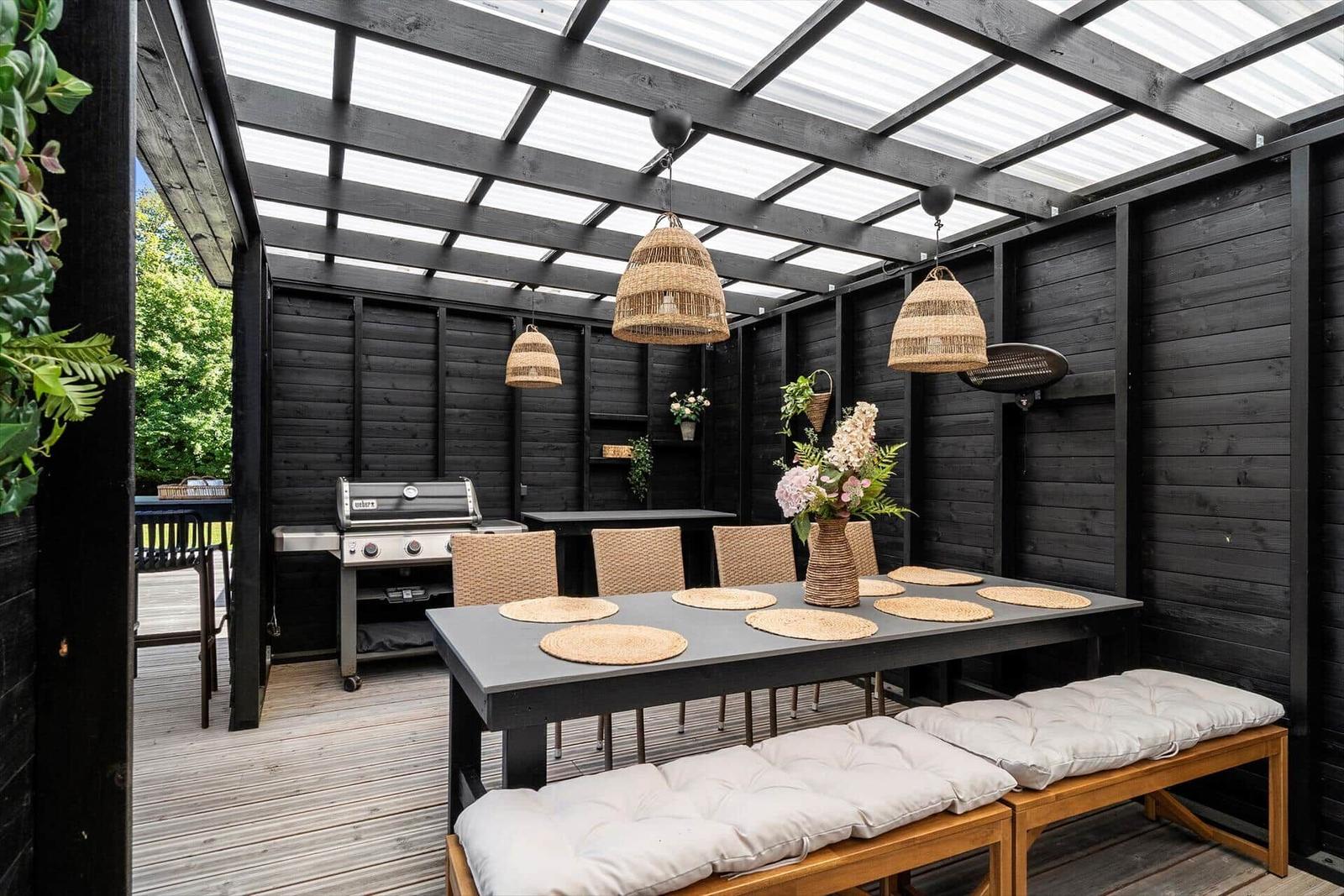 Gartenbereich mit Grill, Esstisch und Sitzbank unter Dach.