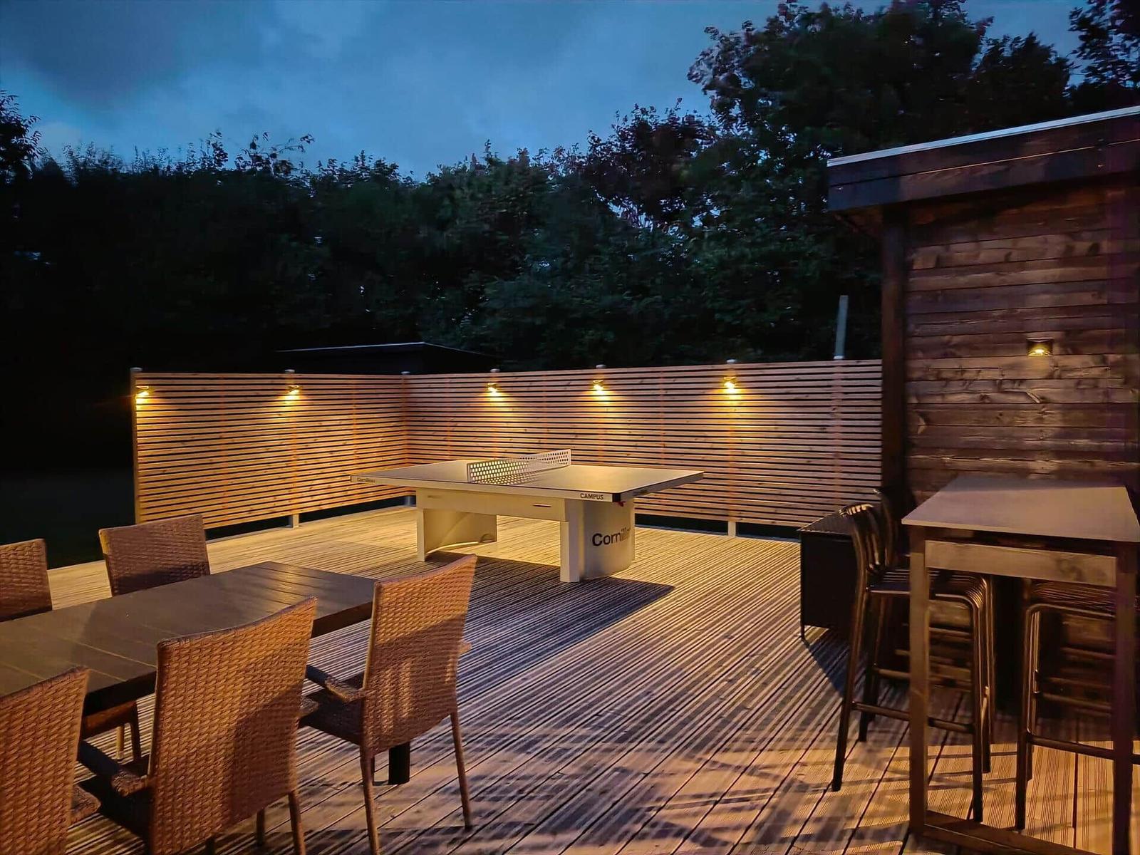 Terrasse mit Tischtennisplatte, Sitzgelegenheiten und Beleuchtung.