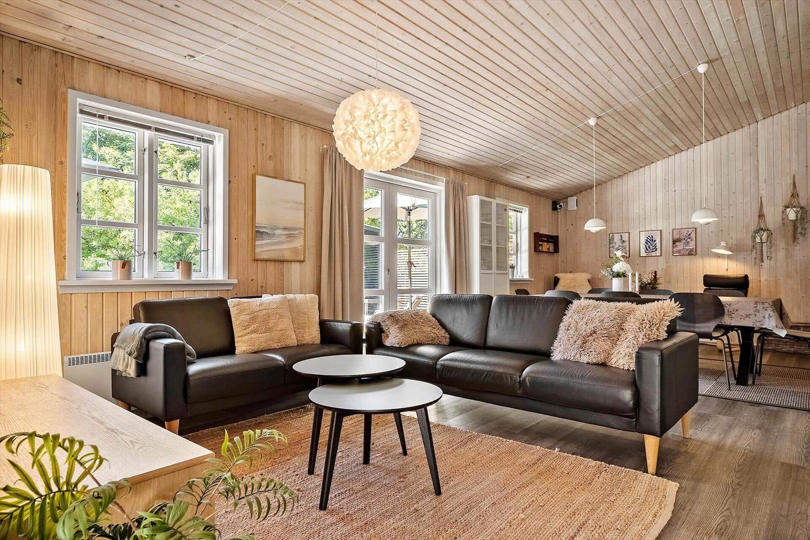 Wohnzimmer mit Holzwänden, zwei schwarzen Sofas und einem runden Tisch.