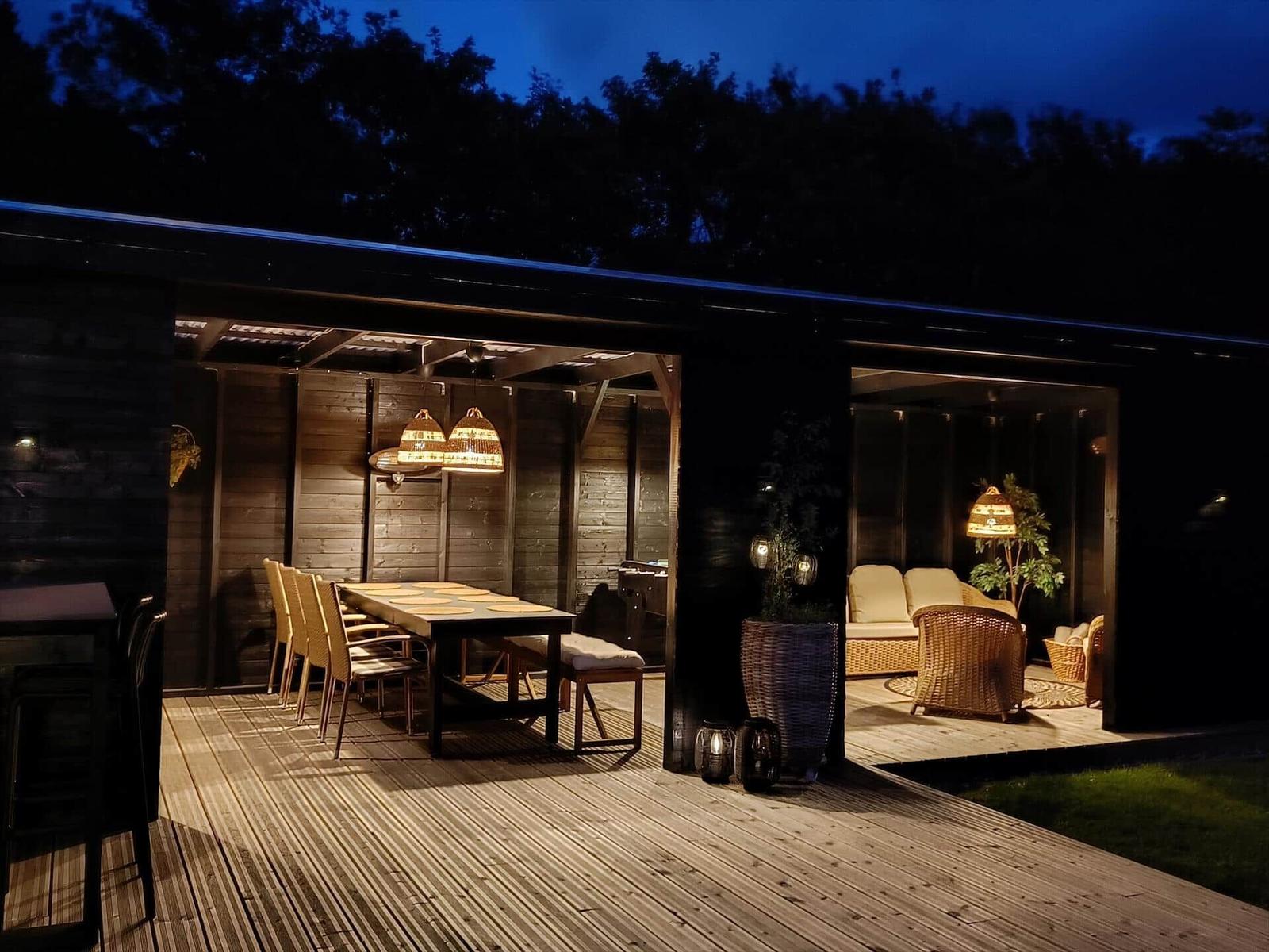 Terrasse mit Essbereich und Loungebereich unter warmen Lichtern.