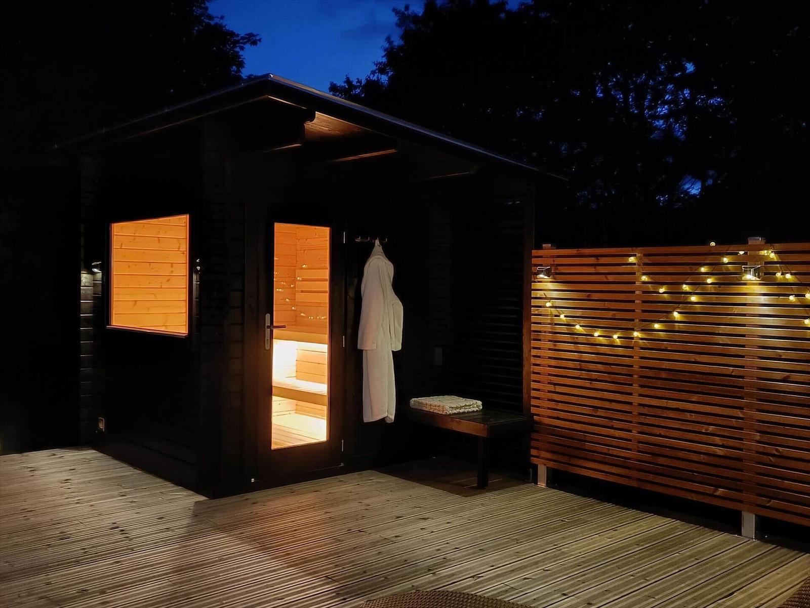 Sauna mit Holzverkleidung und Lichterkette auf Terrasse bei Nacht.