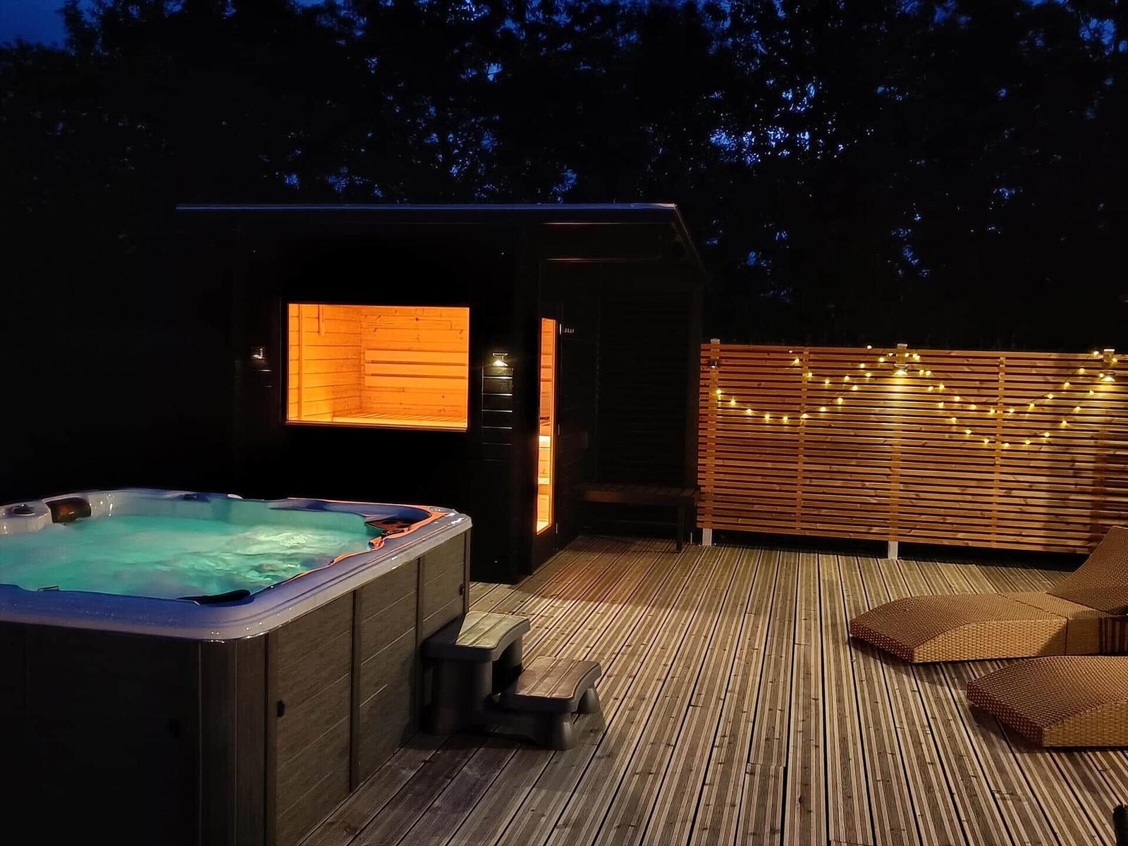 Außenbereich mit Whirlpool, Sauna und Liegen auf Holzterrasse bei Nacht.