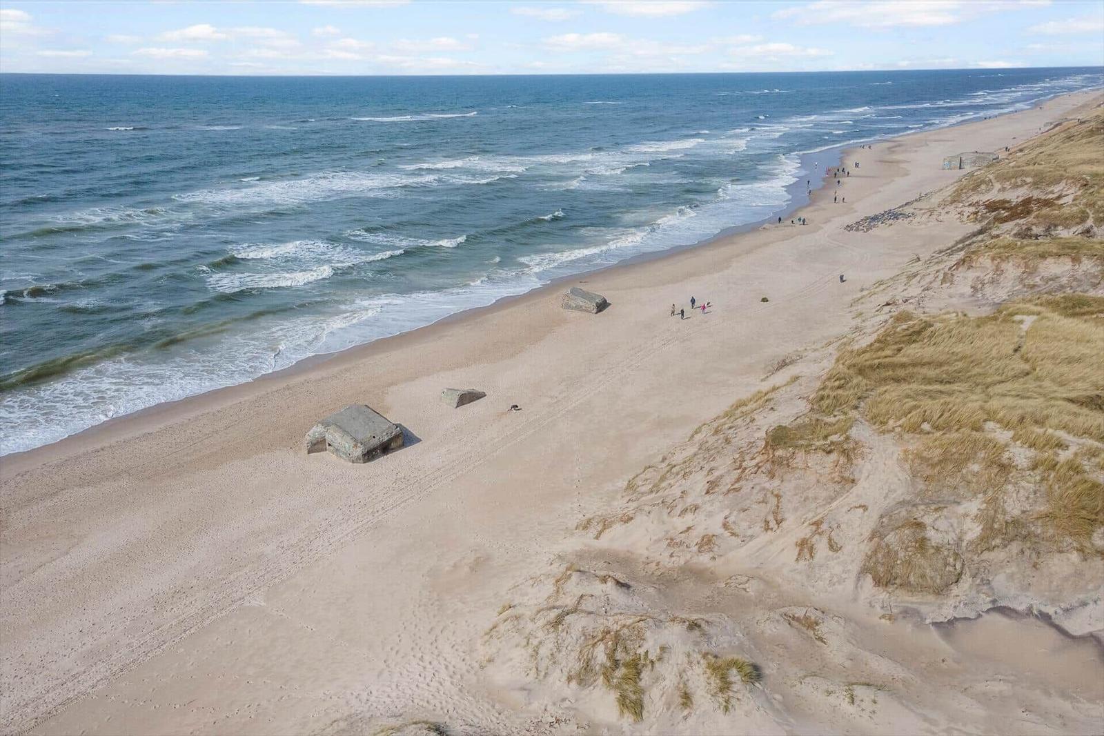 Strand mit Dünen, Wellen und historischen Bunkern.