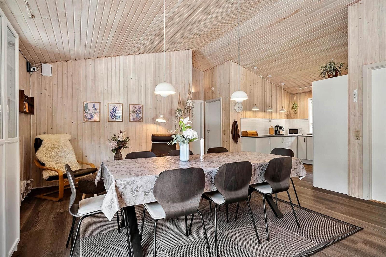 Esszimmer mit Holzwand und Tisch mit Stühlen. Küche im Hintergrund.