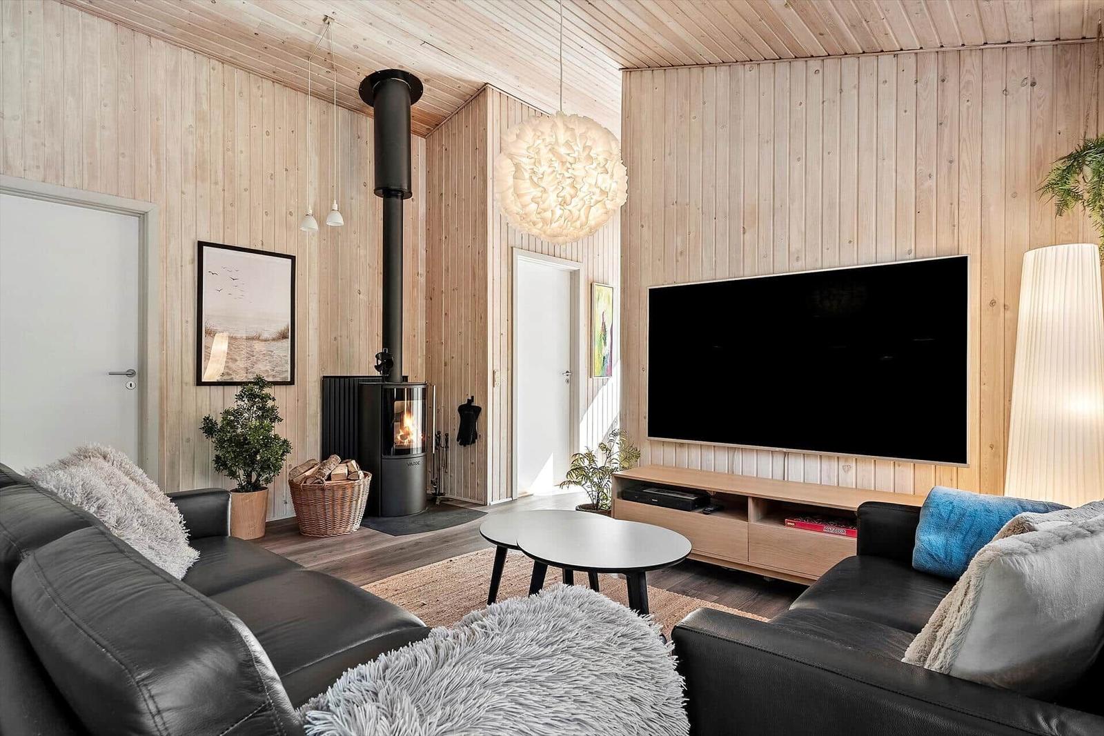 Wohnzimmer mit Holzwand, Kaminofen, Sofa und Fernseher.