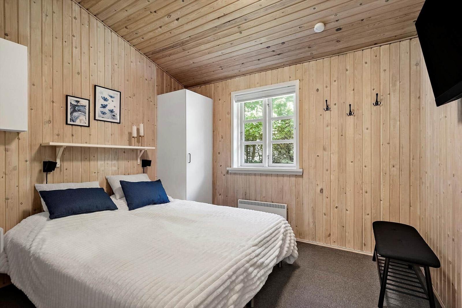 Schlafzimmer mit Holzwänden, Bett, Kleiderständer und Fenster.