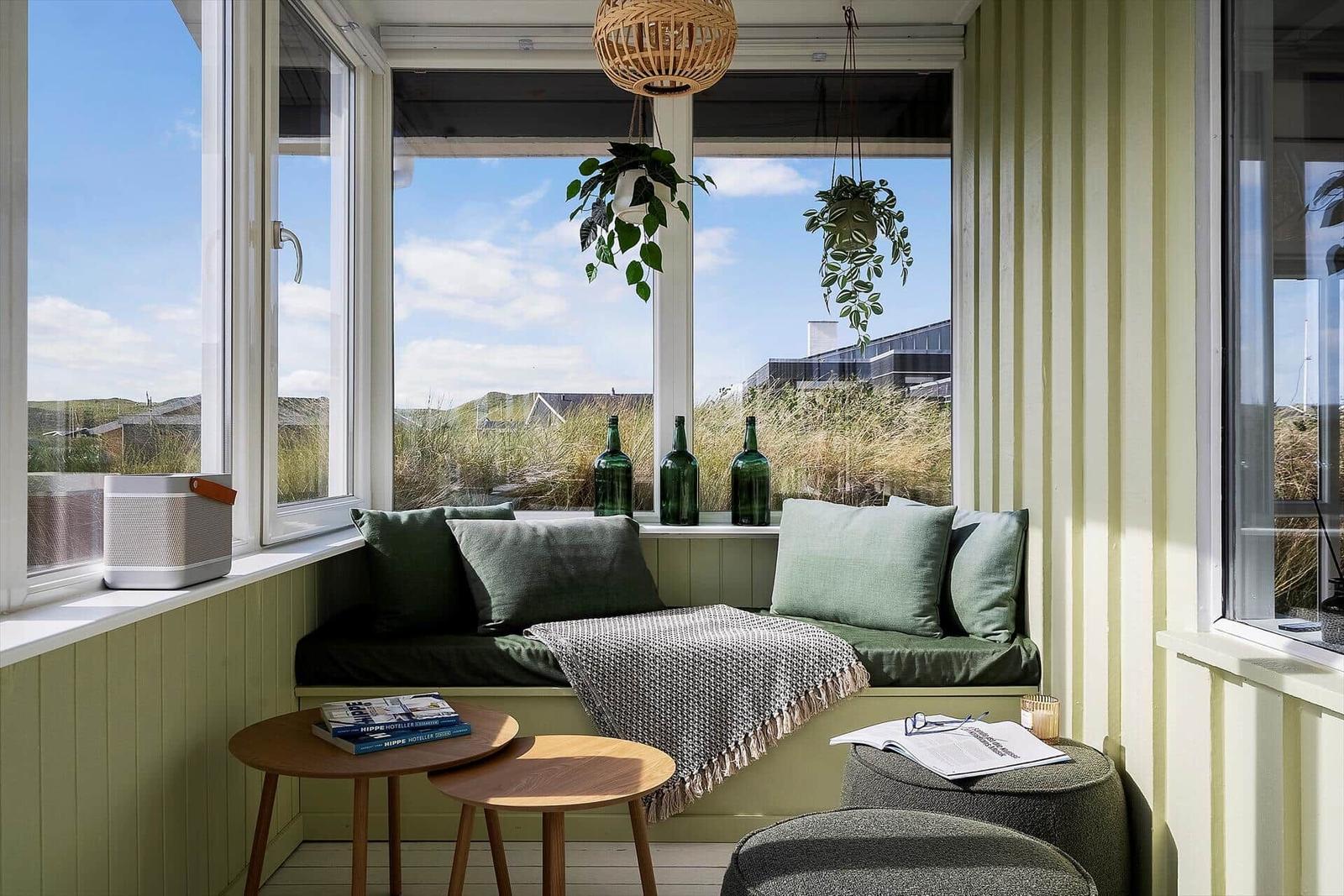 Sitzgelegenheit mit Kissen und Decke vor großem Fenster mit Blick auf Grasland.