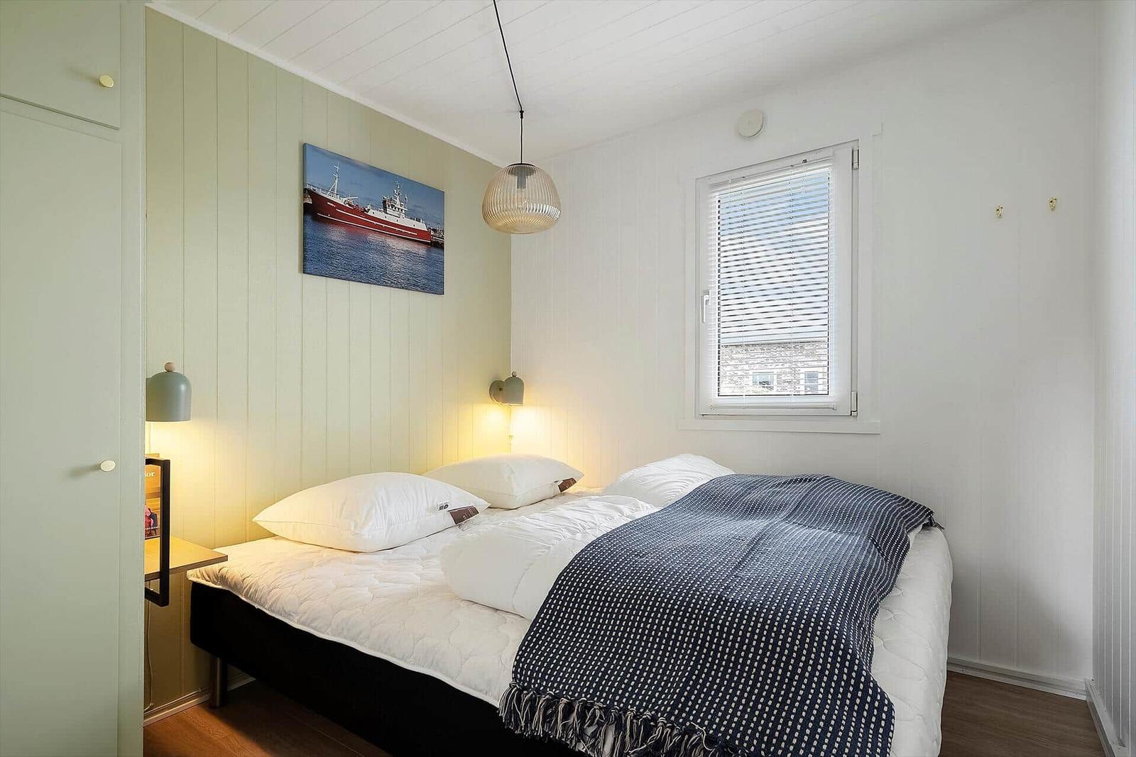 Schlafzimmer mit Bett, Wandbild und Fenster mit Jalousie.