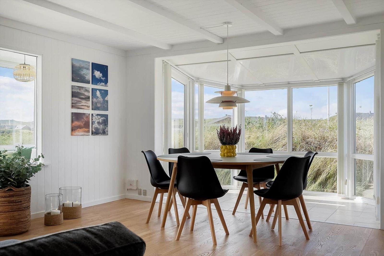 Esszimmer mit runder Tisch, schwarzen Stühlen und großem Fensterblick auf Grasland.