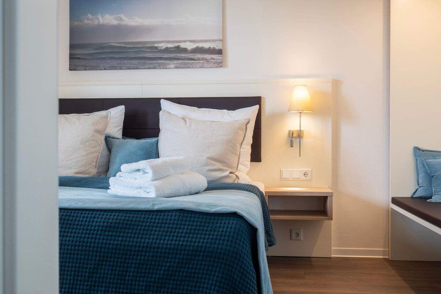 Schlafzimmer mit Bett, Nachttisch und Wandbild. Handtuch auf Bett.