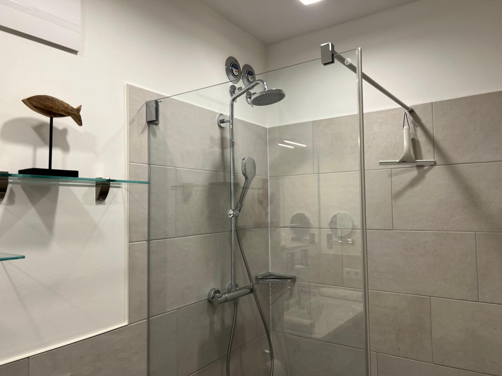 Dusche mit Glaswand und Duschbrause. Wandverkleidung aus hellen Fliesen.