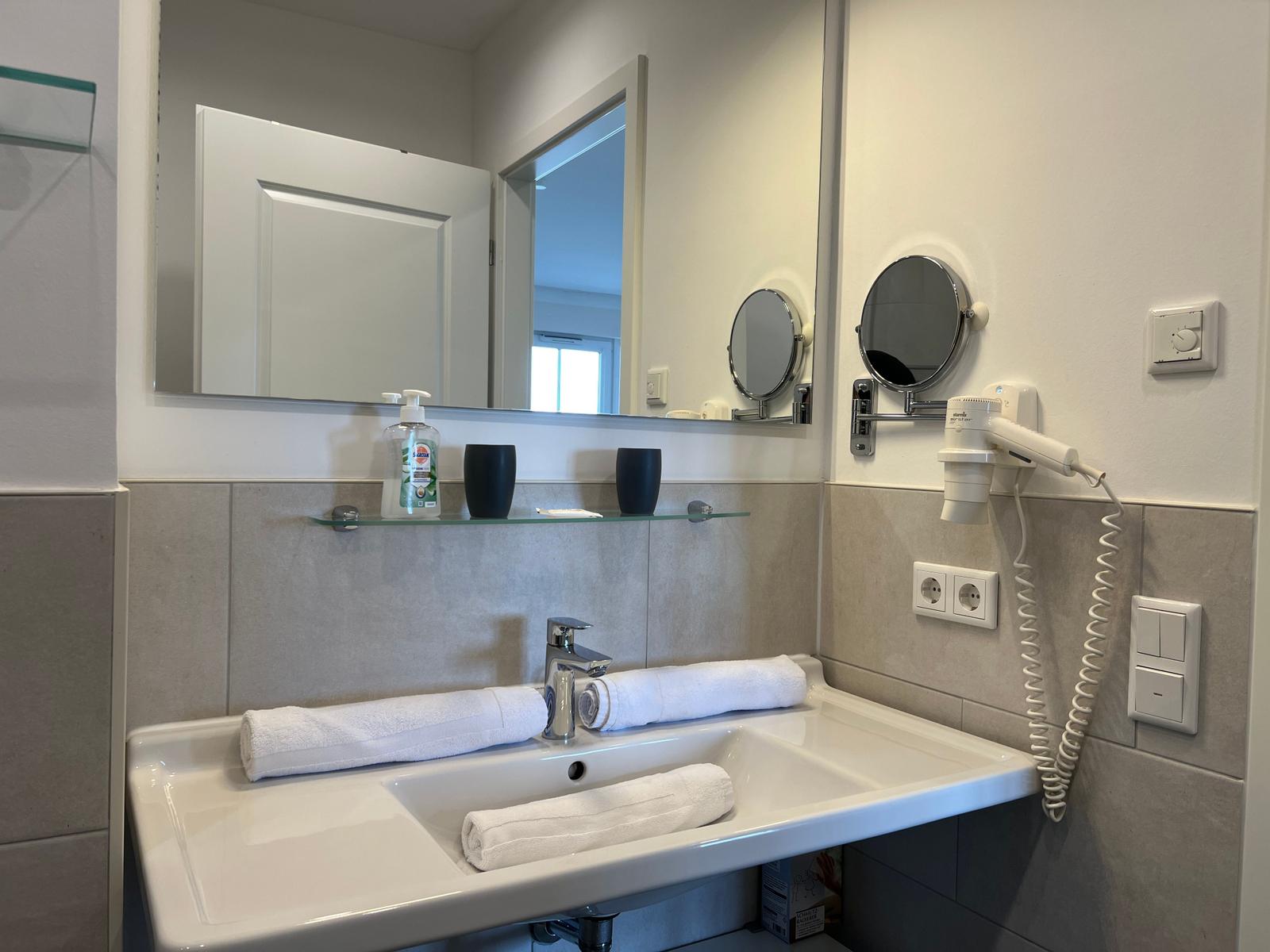 Badezimmer mit Waschbecken, Spiegel und Handtuchhalter.