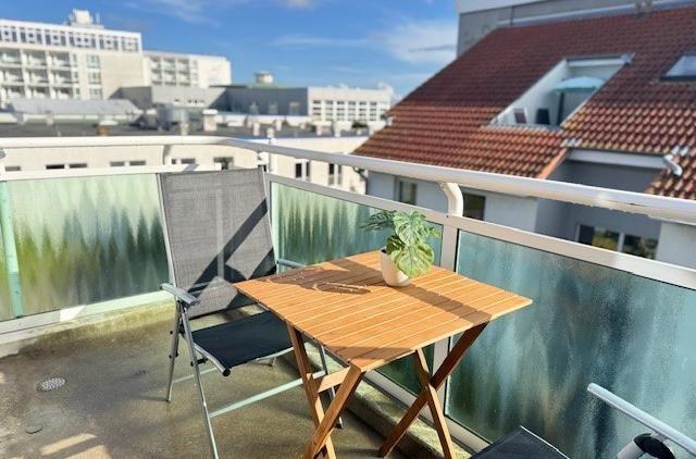 Terrasse mit Tisch, Stuhl und Pflanze. Blick auf Dächer und Gebäude.
