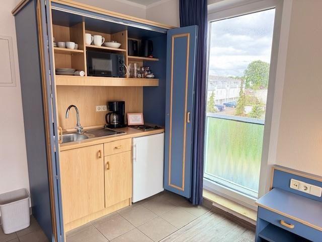 Küche mit Kühlschrank, Mikrowelle und Fenster zum Balkon.