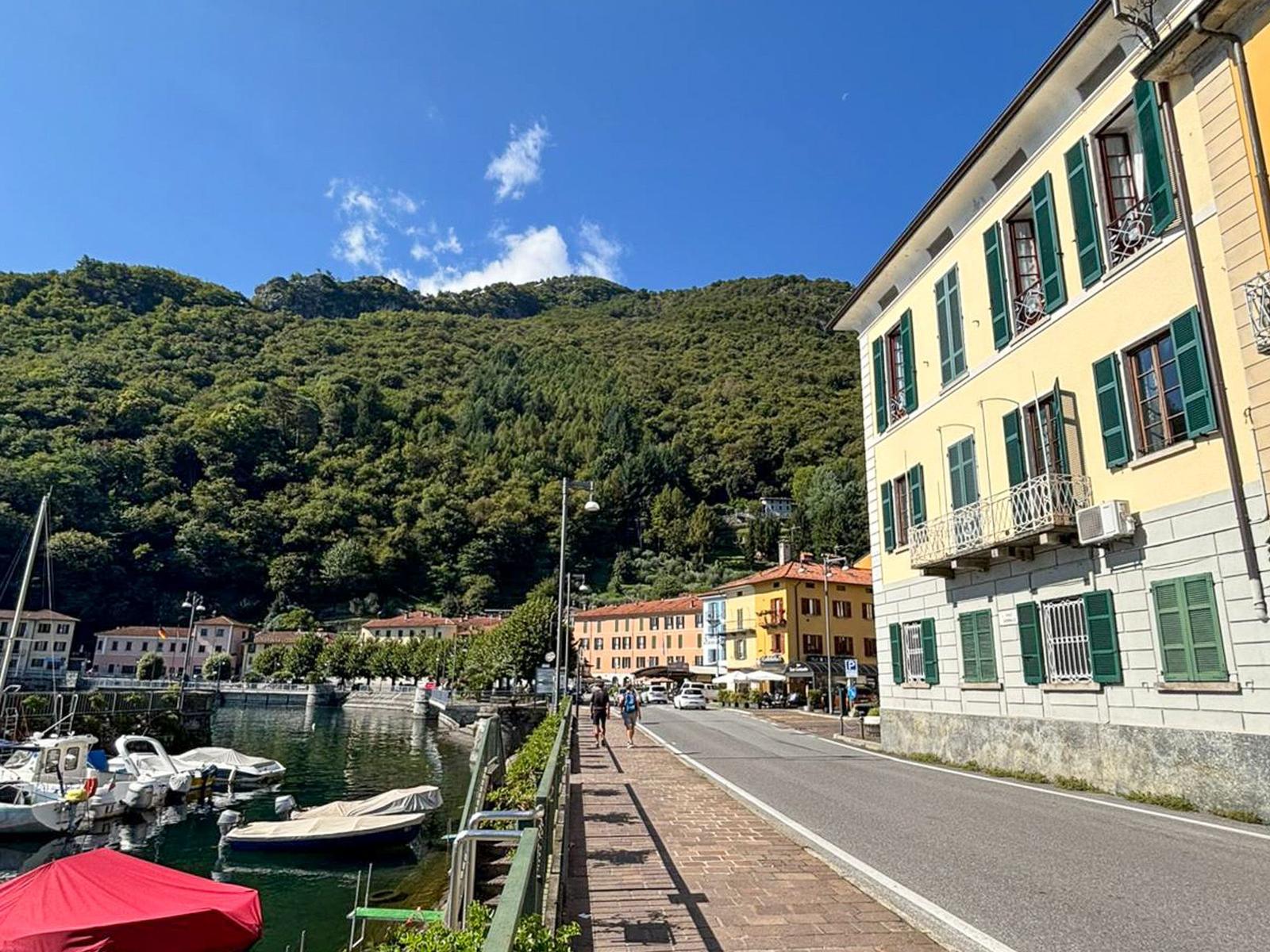Street along the harbor with boats and green hills in the background.