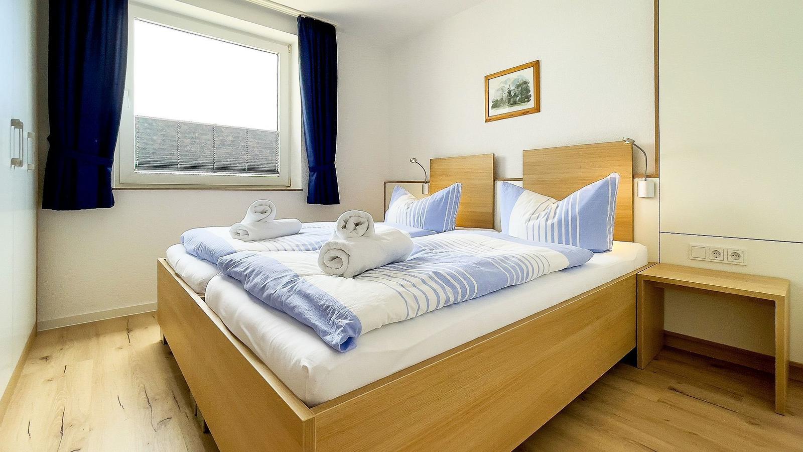 Bedroom with bed, window, and wooden floor. Double bed with blue-white bedding.