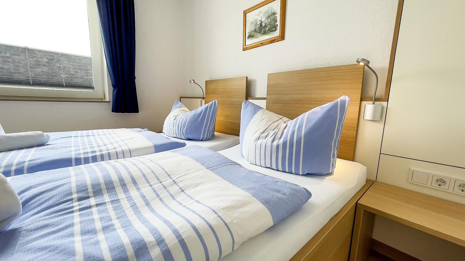 Two single beds with blue and white bedding and wooden frames. Window with blue curtains.