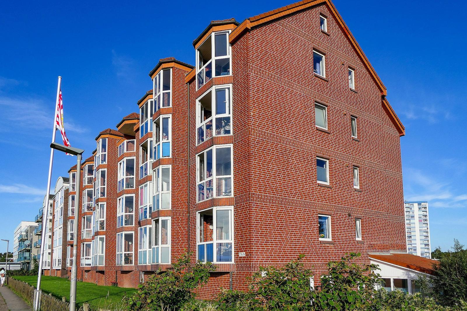Red brick building with white windows and balconies under blue sky.