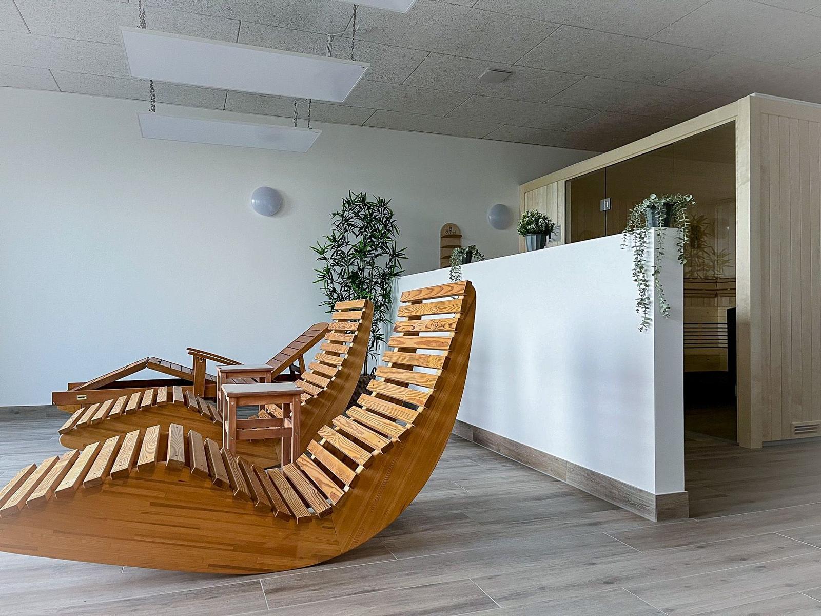 Living area with wooden loungers and sauna in the background.