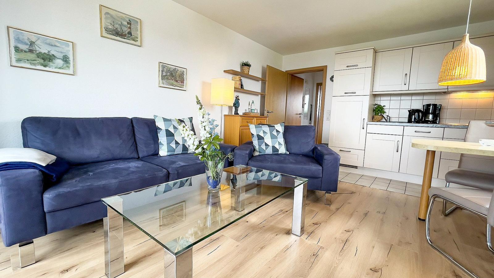 Living room with sofa, couch and glass table. Kitchen with white cabinets and dining table.