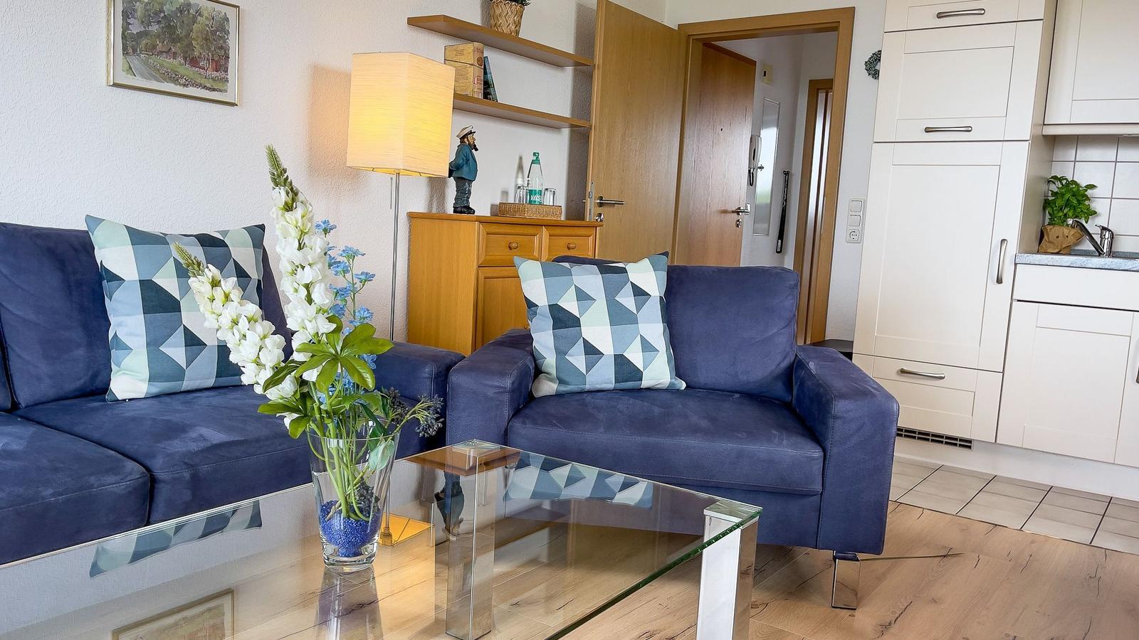 Living room with blue sofa, glass table, and kitchen area.