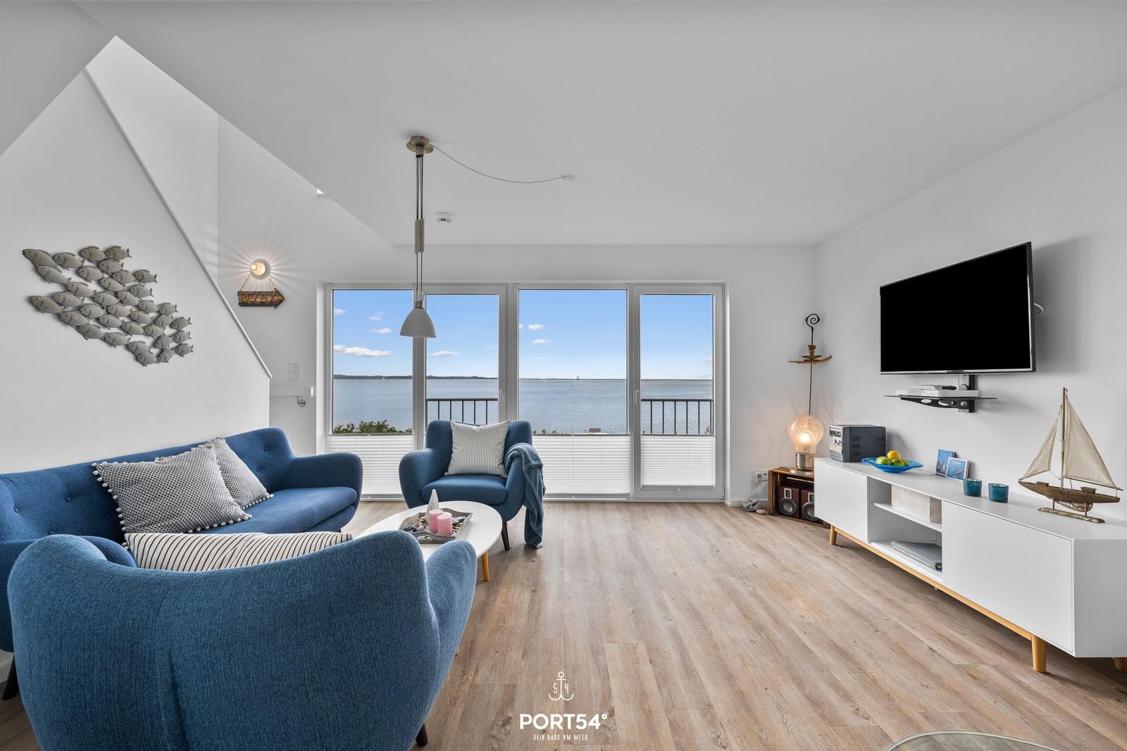 Wohnzimmer mit Blick aufs Wasser, blauer Sofa, TV und Stehregal.