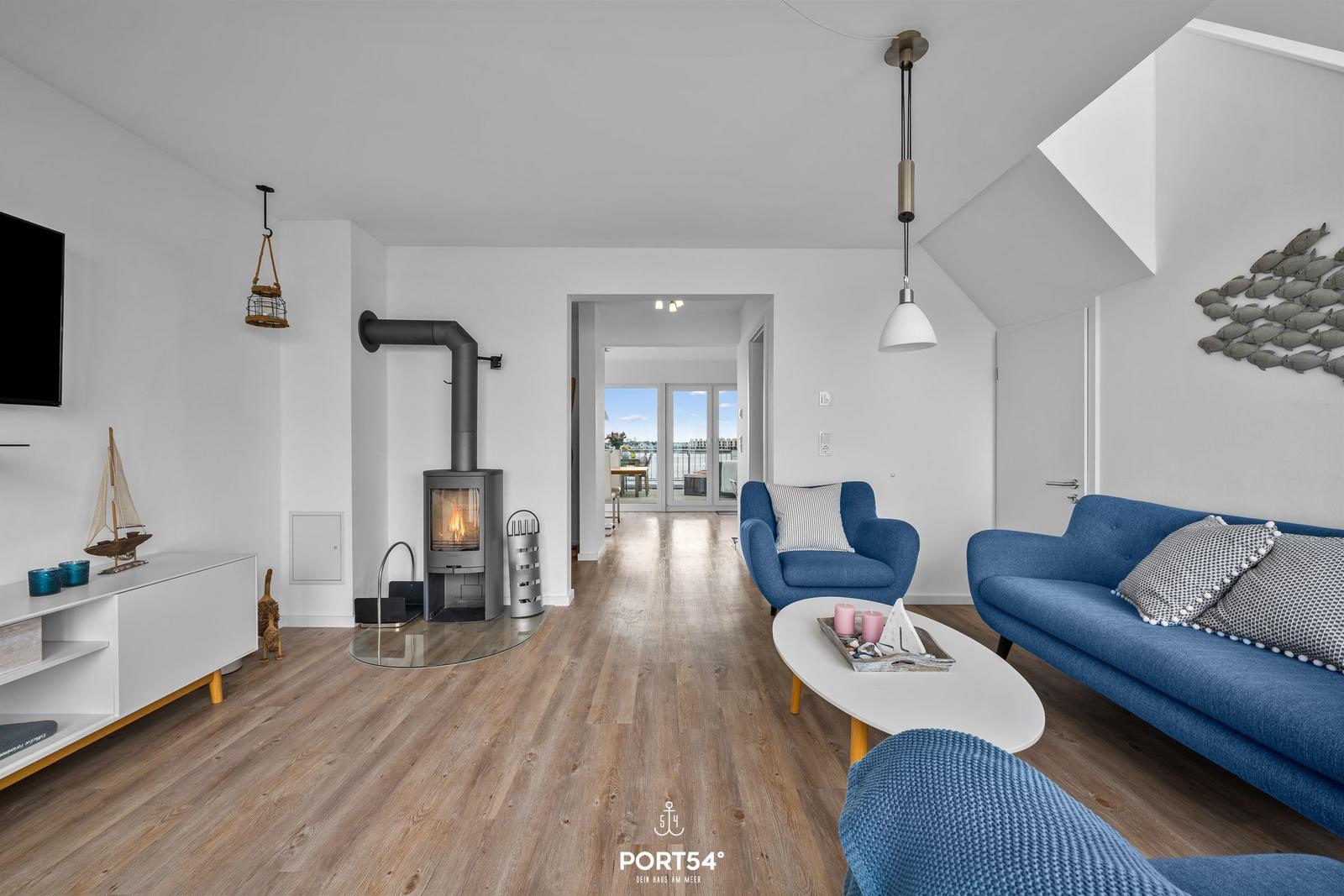 Wohnzimmer mit Kamin, blauer Couch und Holzboden. Durchgang zur Terrasse.