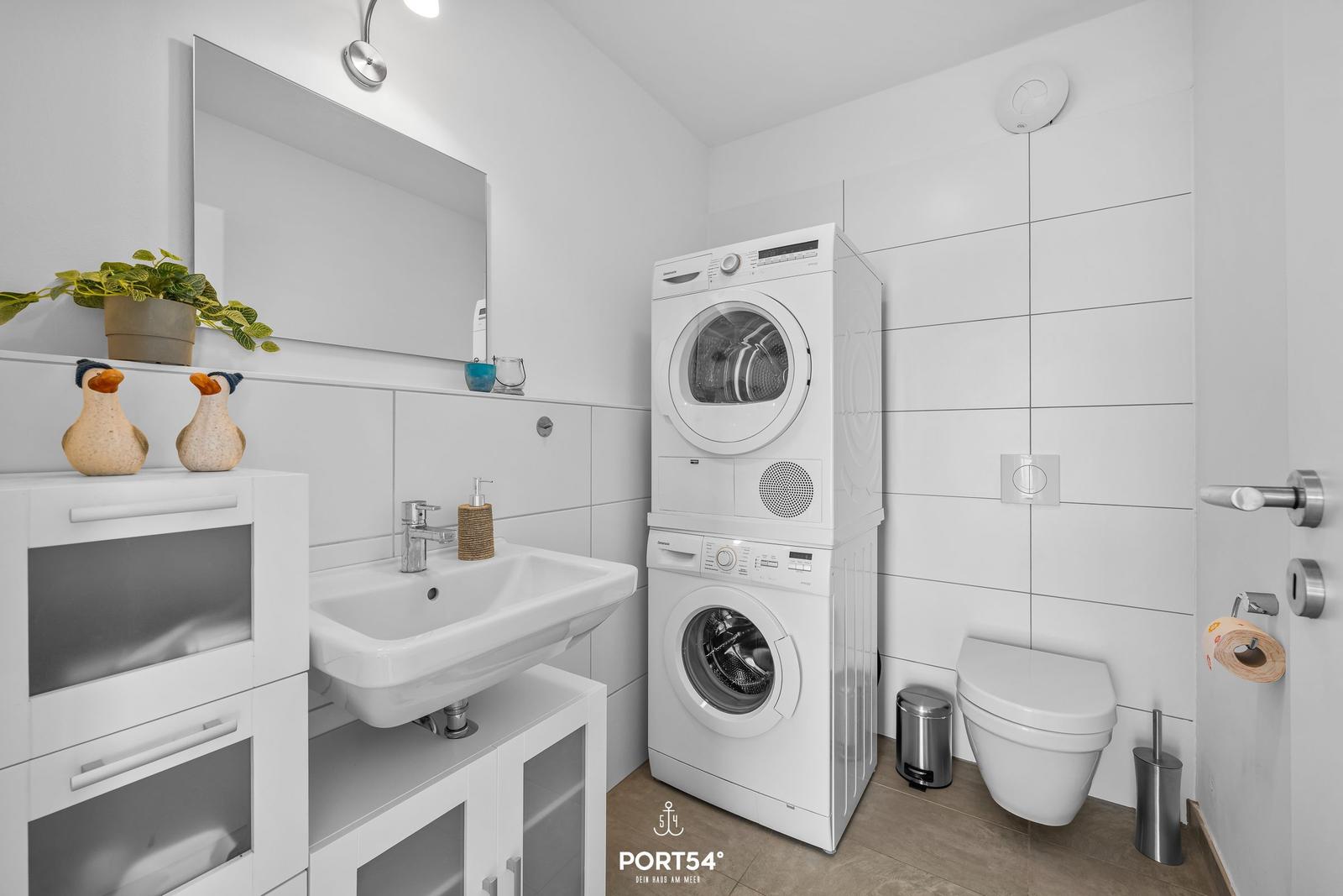 Badezimmer mit Waschmaschine, Trockner, Toilette und Spiegel.