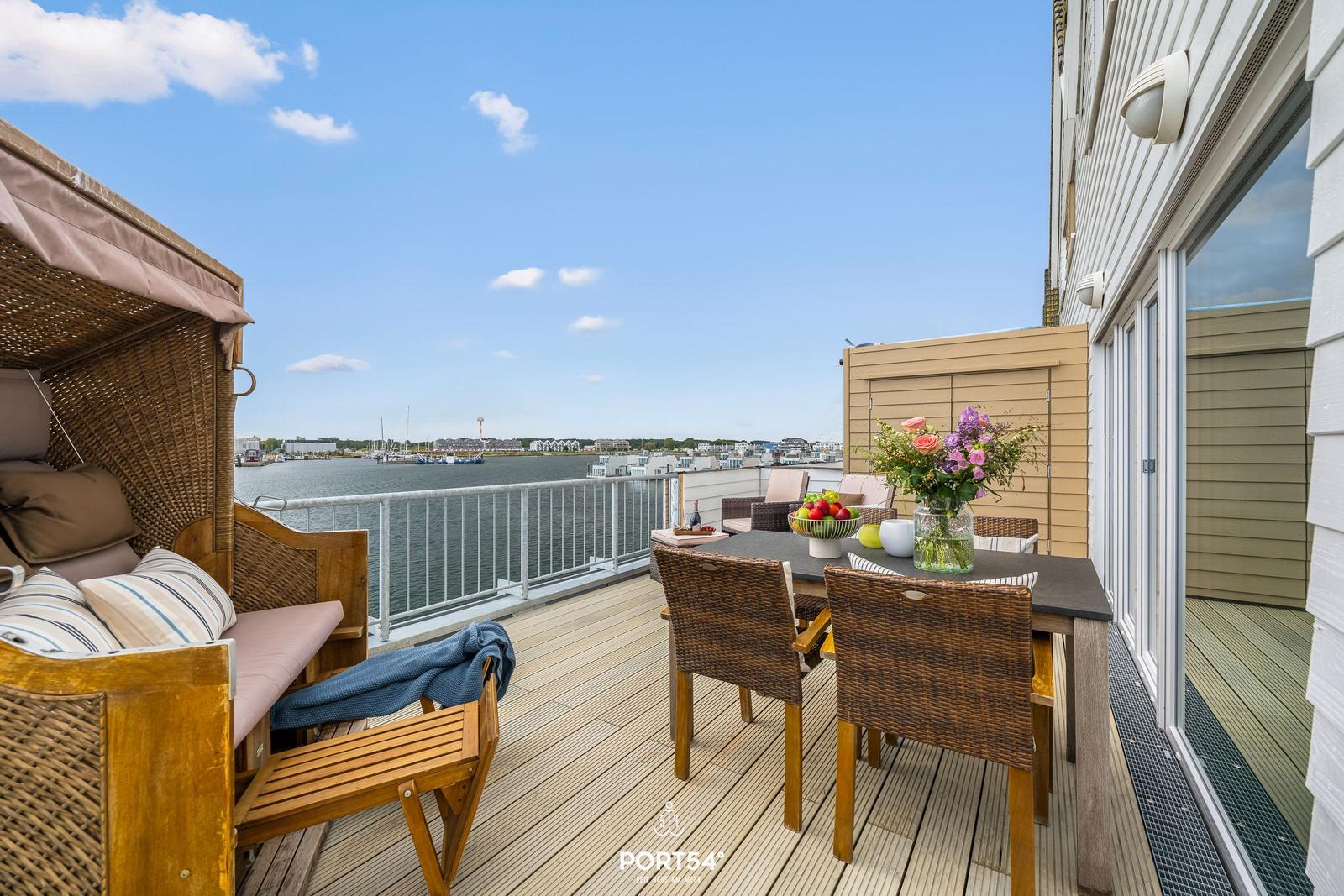 Terrasse mit Sitzgelegenheiten und Meerblick. Tisch mit Blumen und Obst.