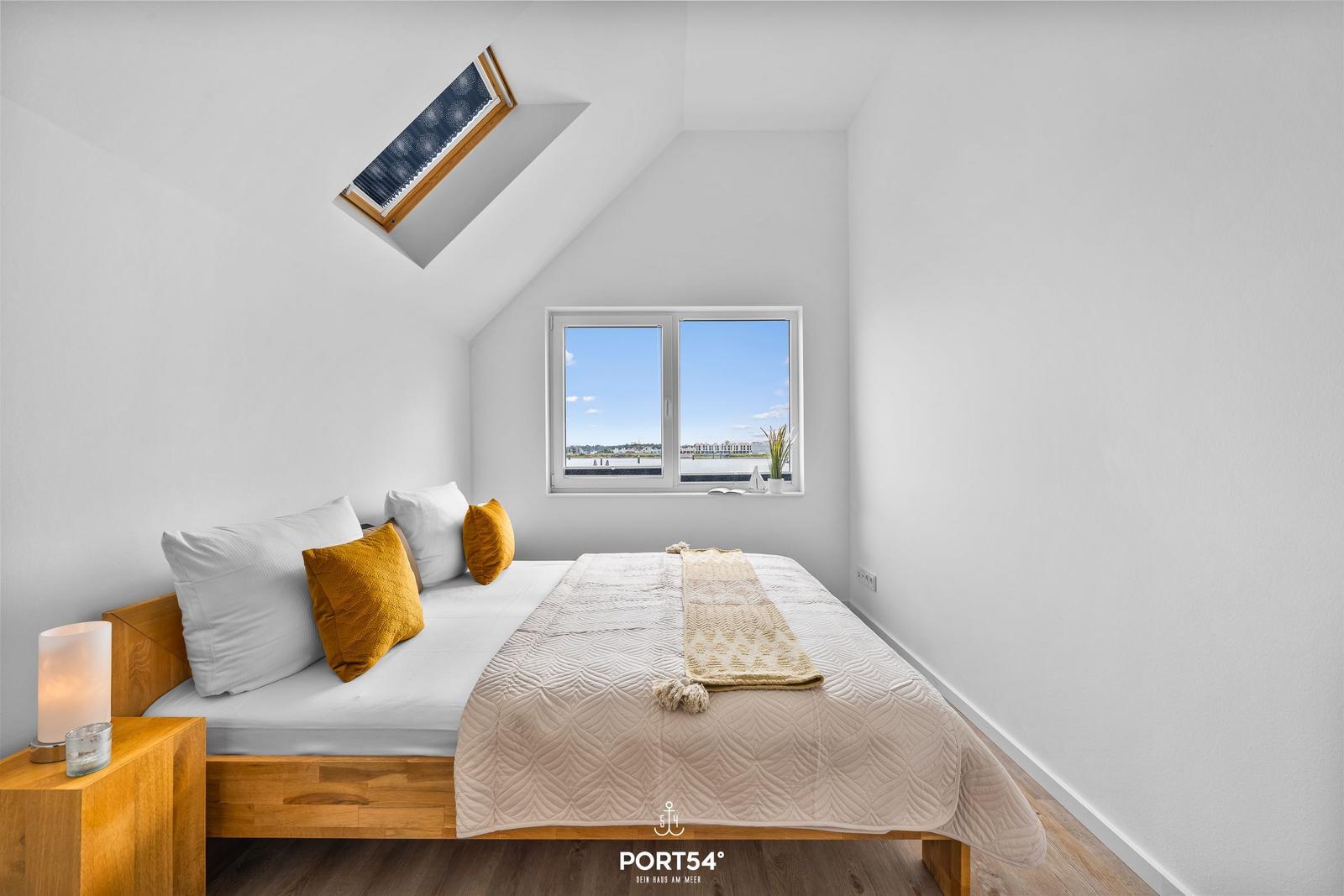 Schlafzimmer mit Dachfenster und Blick auf Wasser.