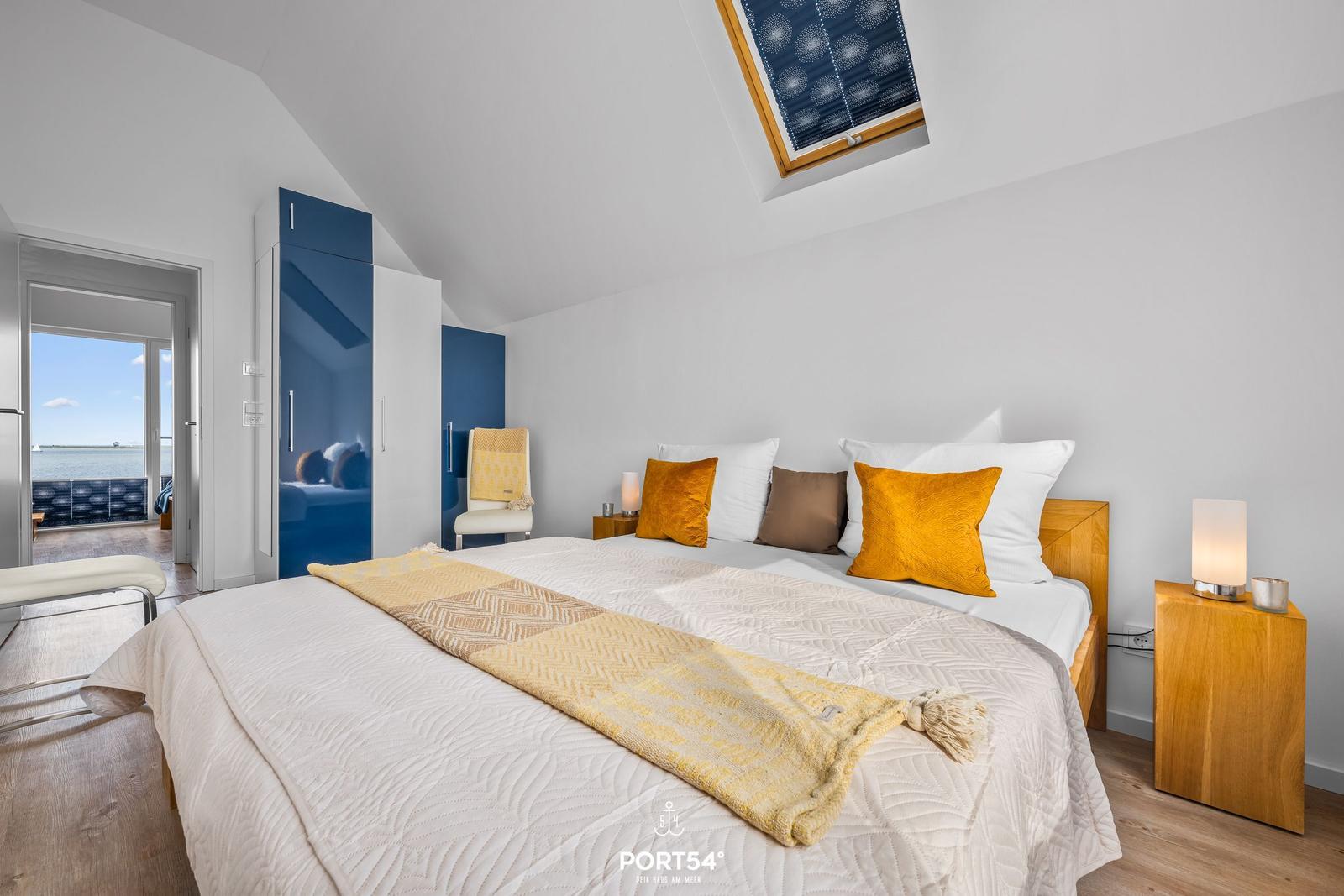 Schlafzimmer mit Blick auf Wasser, Dachfenster und blauer Schrank.