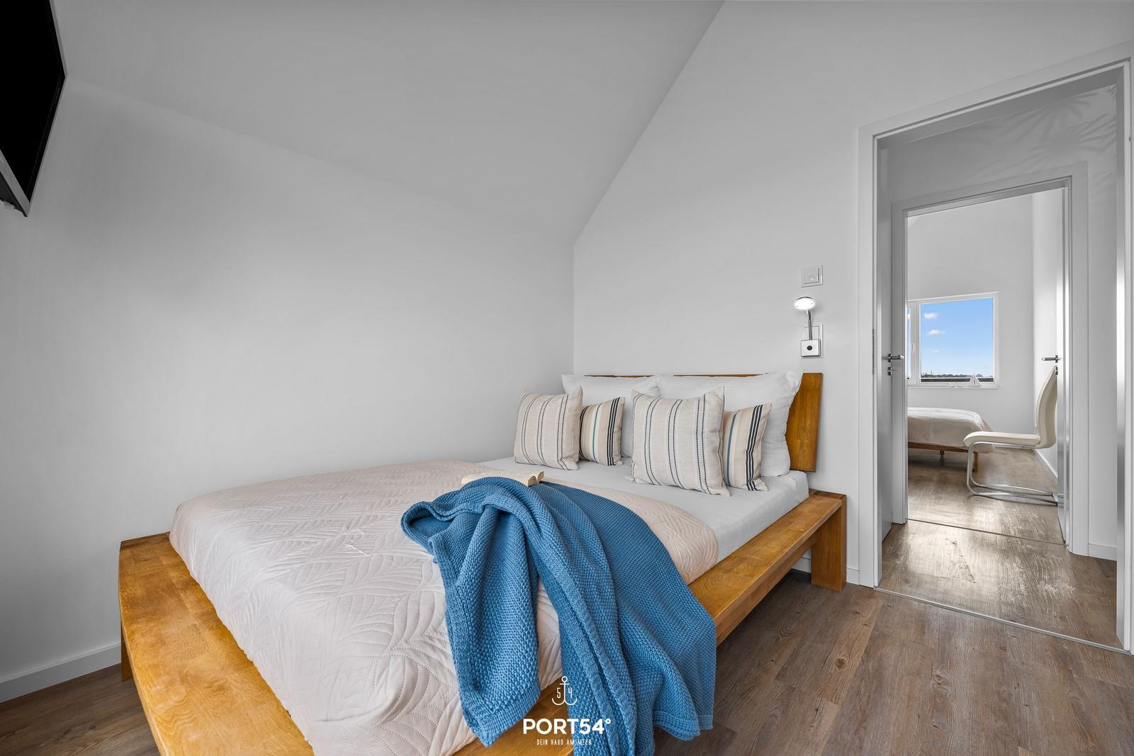 Schlafzimmer mit Holzbett, blauer Decke und Blick in angrenzenden Raum.